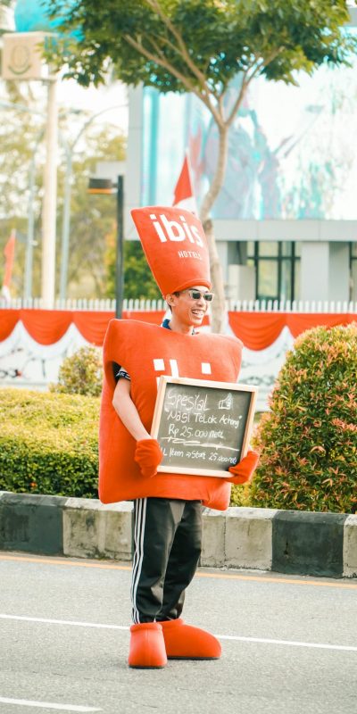 Person wearing a red costume holding a sign promoting a restaurant offer on a street.