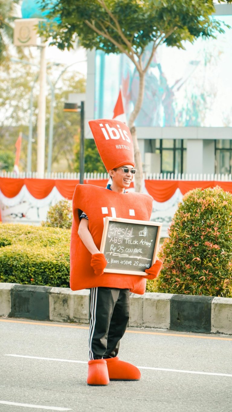 Person wearing a red costume holding a sign promoting a restaurant offer on a street.